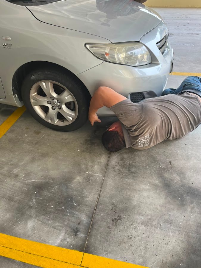 Inspetor no chão olhando a parte inferior de um carro prata